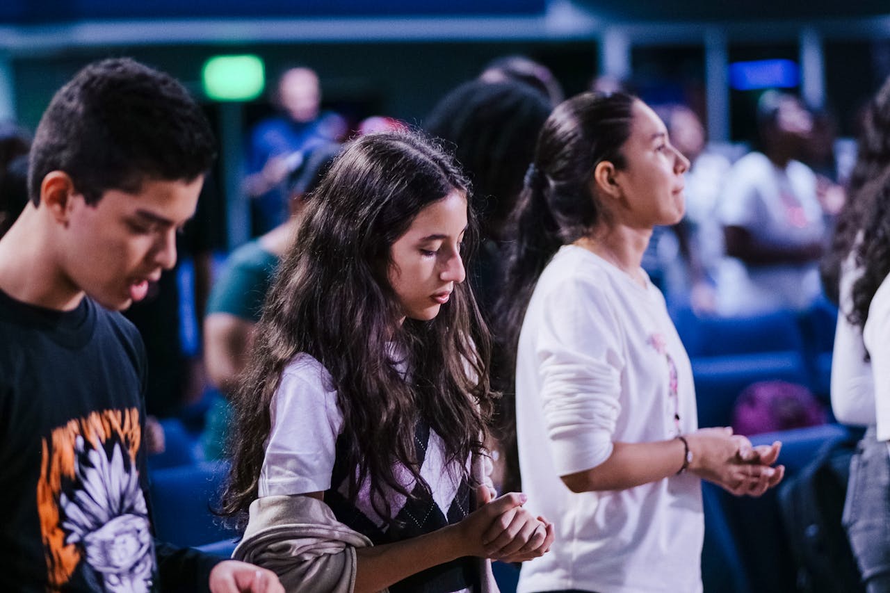 A diverse group of young individuals deep in prayer during a church service indoors, fostering community spirit.